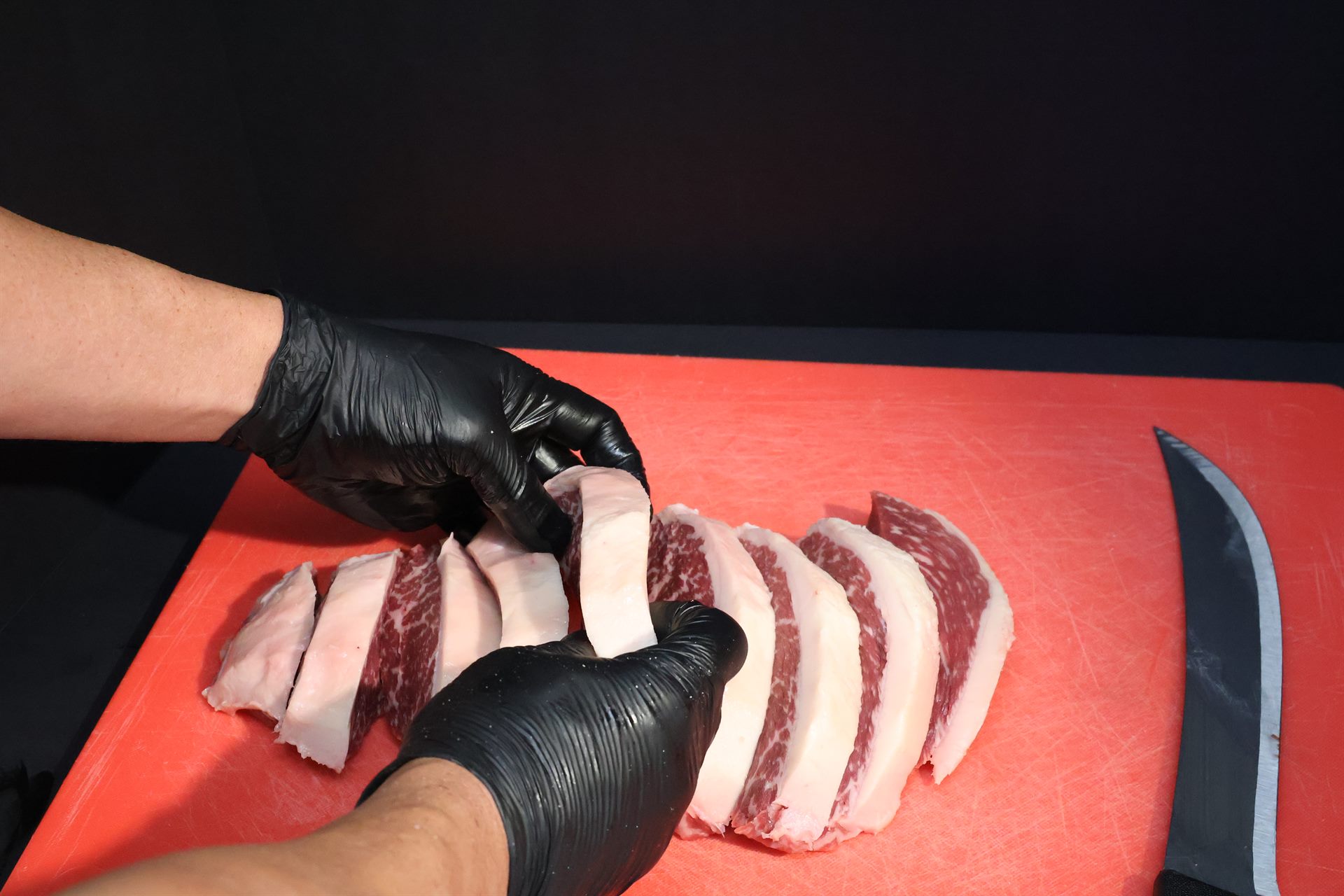A butcher in black gloves slices marbled steaks on a red board at the Vitoria counter